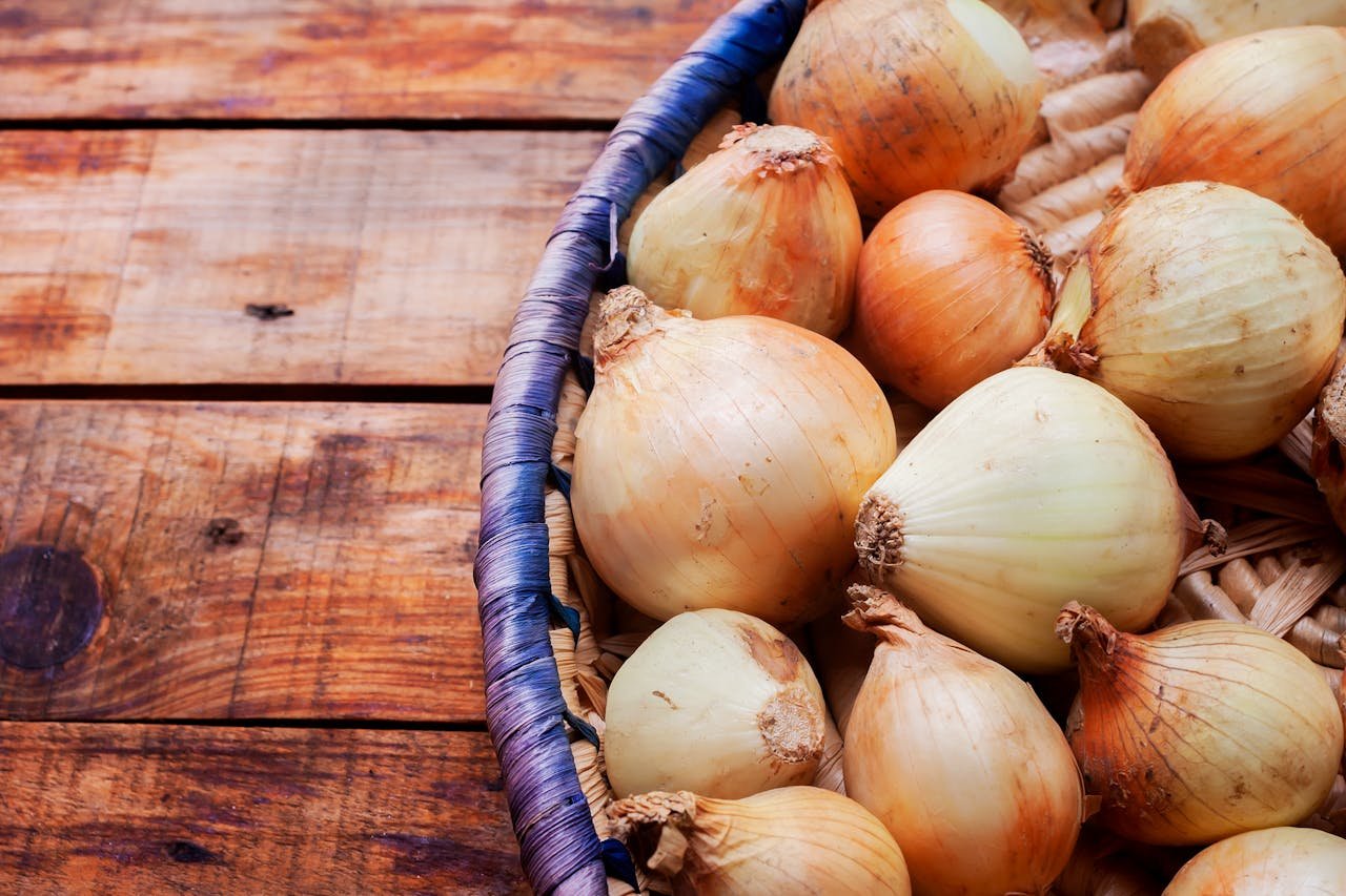 Fresh whole onions in a woven basket on a rustic wooden table, perfect for culinary themes.